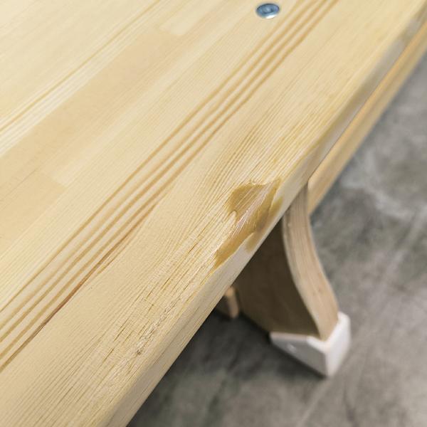 Holztisch mit sichtbarem Wasserschaden und aufgequollenem Lack an der Ecke.