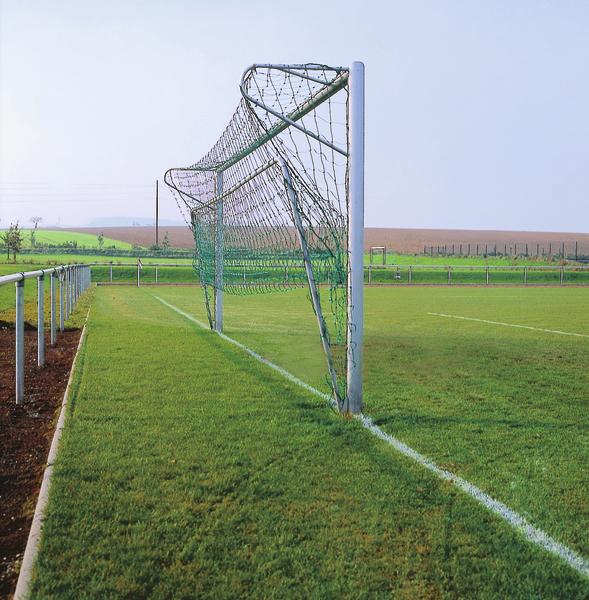 Leeres Fußballtor mit Netz auf grünem Spielfeld in ländlicher Umgebung.