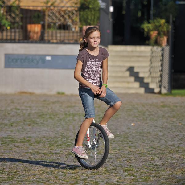 Mädchen fährt Einrad auf gepflastertem Platz im Freien bei Sonnenschein.