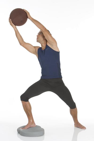 Mann trainiert mit Medizinball auf Balancekissen, Ganzkörper-Workout für Kraft und Stabilität.