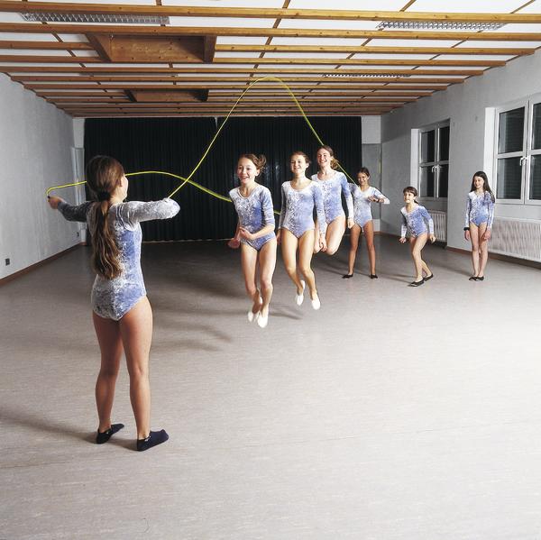 Mädchen in Turnanzügen springen gemeinsam Seil in einem hellen Trainingsraum.