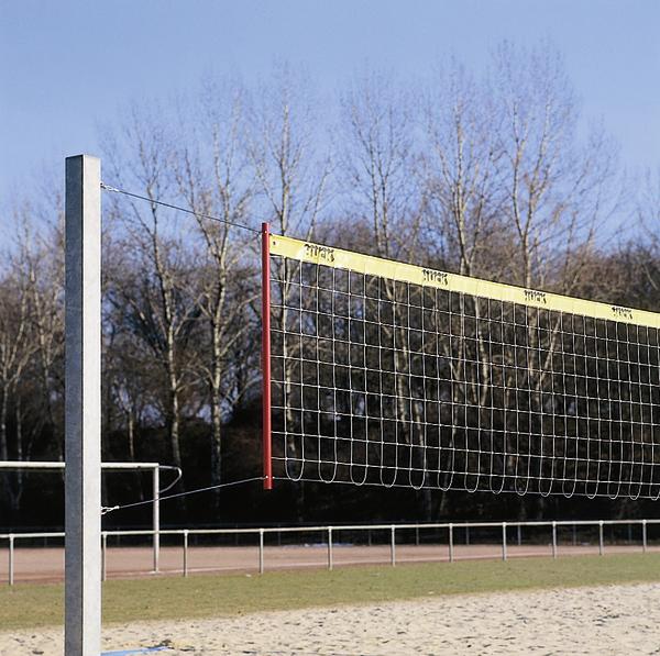 Volleyballnetz auf Sandplatz im Freien vor kahlen Bäumen und blauem Himmel.