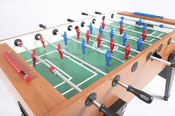 Tischkicker mit roten und blauen Spielfiguren auf grünem Spielfeld, Holzrahmen.