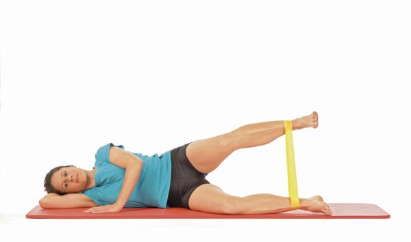 Frau macht seitliche Beinübung mit Widerstandsband auf Fitnessmatte, Ganzkörpertraining.