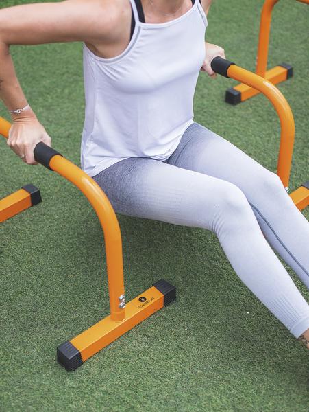 Frau trainiert Dips an orangen Fitnessbarren auf grünem Outdoor-Sportplatz.