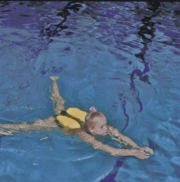 Kind schwimmt mit Schwimmhilfe im klaren blauen Wasser eines Schwimmbeckens.