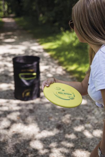 Frau wirft gelbe Frisbee-Scheibe auf Outdoor-Wurfspiel mit Zielkorb im Park.