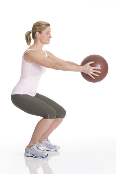Frau macht Kniebeuge mit Medizinball, Fitnessübung für Beine und Rumpf.