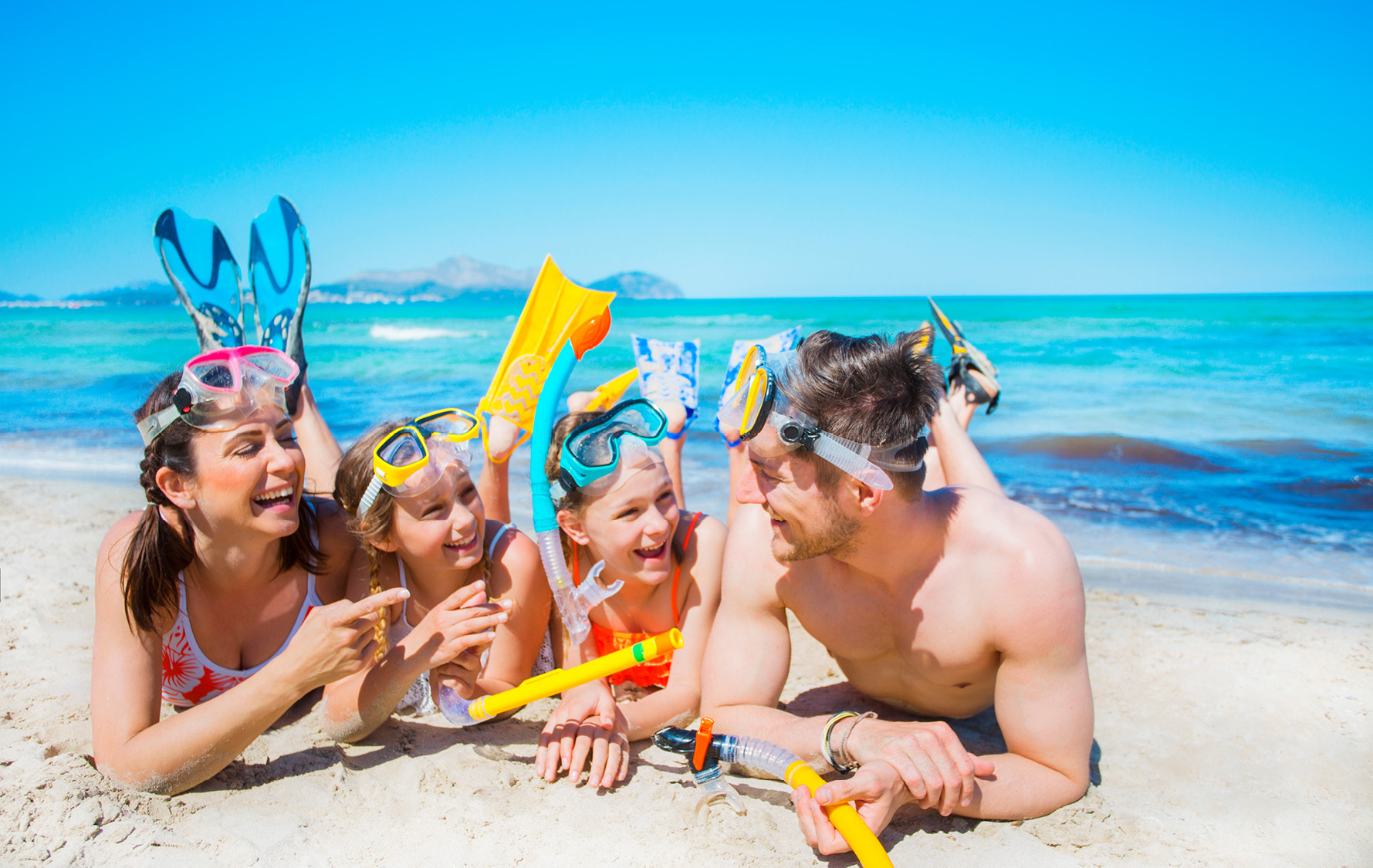 Familie liegt am Sandstrand und trägt Taucherequipment