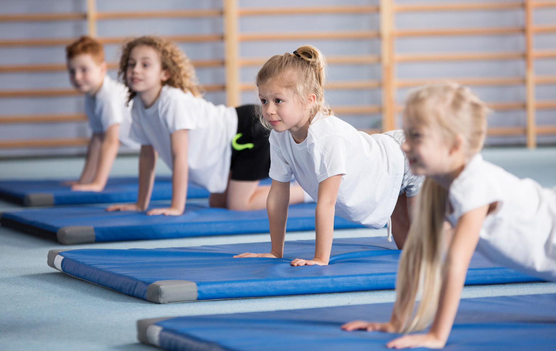 Vier Kinder liegen in einer Sporthalle auf blauen Turnmatten und stützen sich mit den Händen ab.